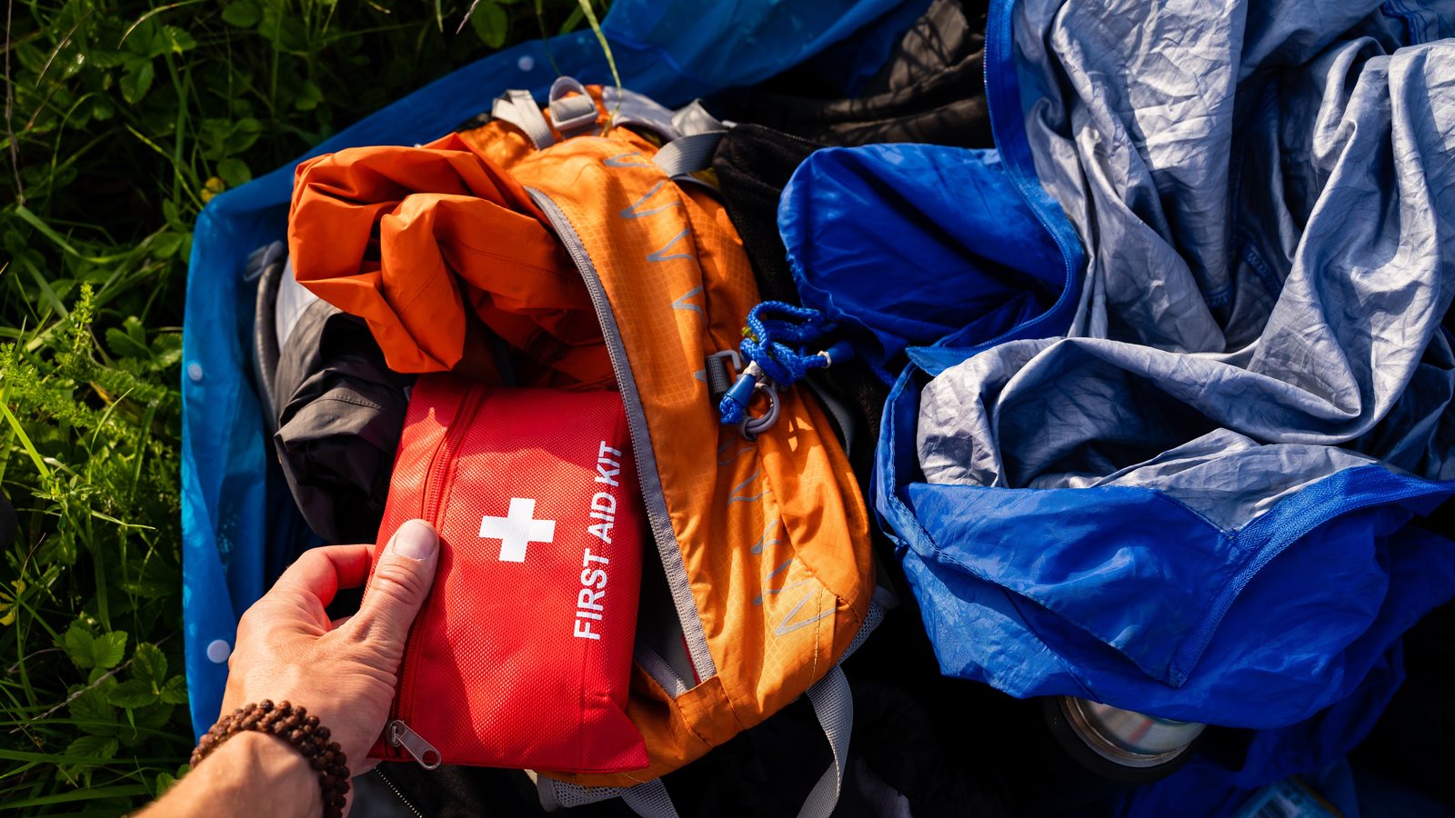 A first-aid pouch held in hand beside packed rucksacks