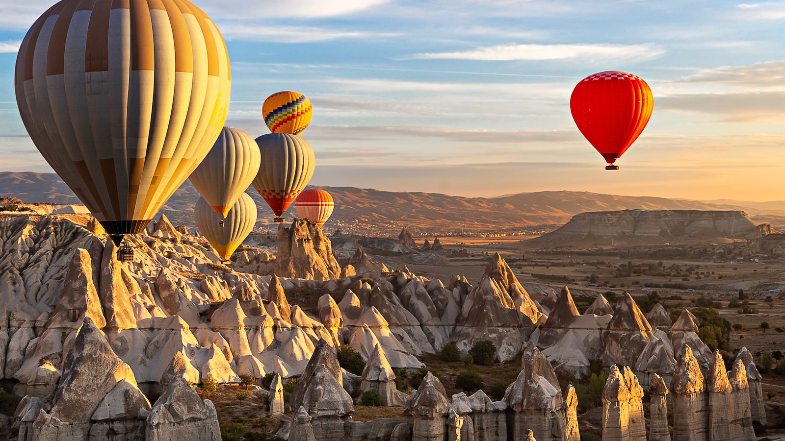 Hot-air balloons drifting over fairy chimneys in the first light, with the plateau beyond