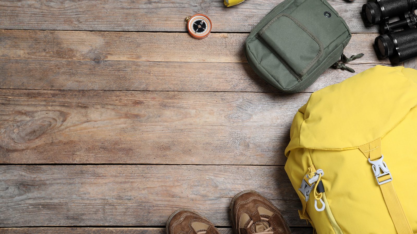 Walking shoes, a yellow rucksack, torch, compass and binoculars laid out on a wooden table